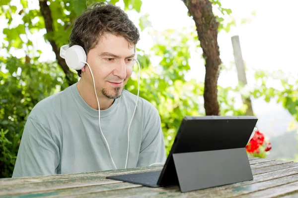 Joven que trabaja con una tableta PC con auriculares, al aire libre —  Fotos de Stock