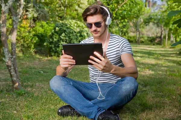 Uomo casual che tiene un tablet con cuffie, all'aperto — Foto Stock