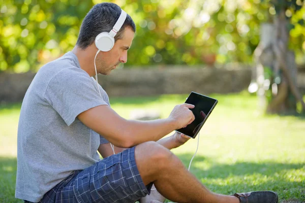 Giovane che si rilassa con un tablet pc ascoltando musica con le cuffie — Foto Stock