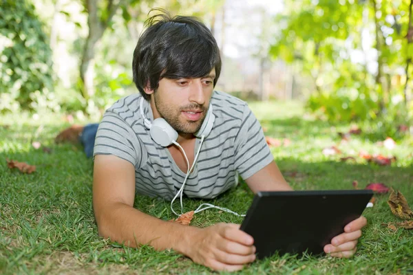 Giovane che si rilassa con un tablet pc ascoltando musica con le cuffie — Foto Stock