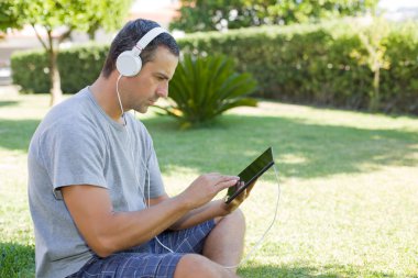 genç adam bir kulaklık ile müzik dinleme tablet pc ile rahatlatıcı bir parkta