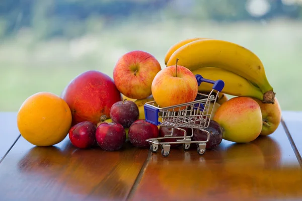 Mängd frukt och en liten kundvagn på bordet i trädgården — Stockfoto