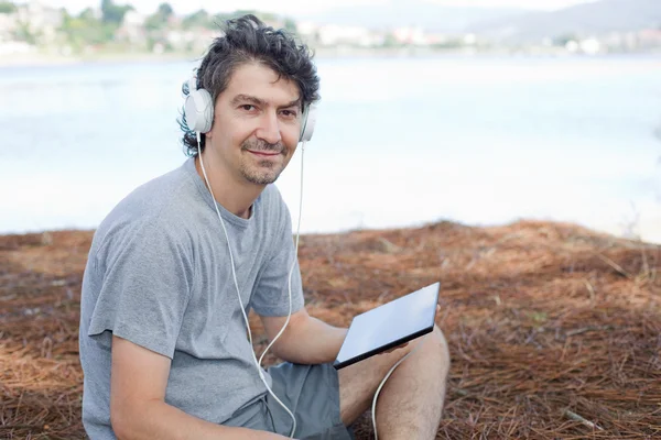 Joven sosteniendo una tableta con auriculares, en la playa — Foto de Stock
