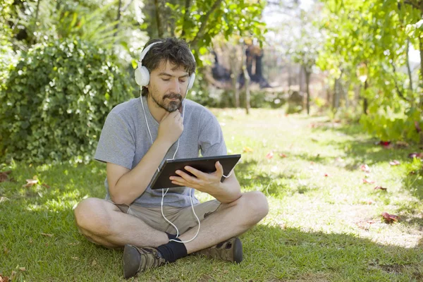 Jovem segurando um tablet com fones de ouvido, ao ar livre — Fotografia de Stock