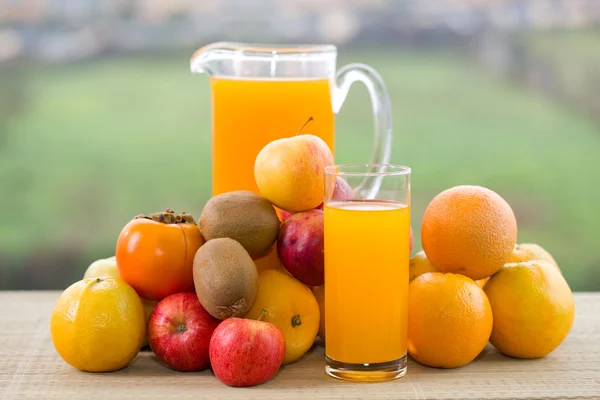 Vasos de jugo de naranja y muchas frutas en la mesa de madera al aire libre —  Fotos de Stock