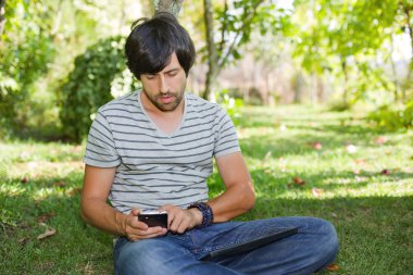 genç adam bir tablet pc ile rahatlatıcı ve üzerinde telefon bir parkta, açık