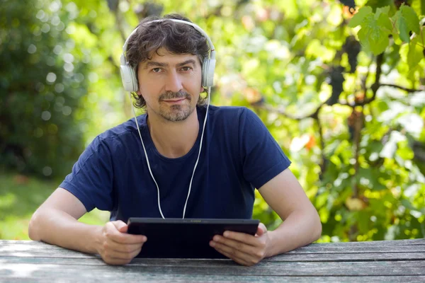 Jovem segurando um tablet com fones de ouvido, ao ar livre — Fotografia de Stock