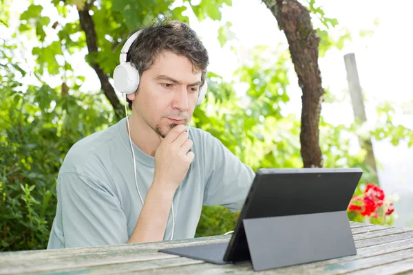 Young man working with a tablet pc listening music with headphones — Stock Photo, Image