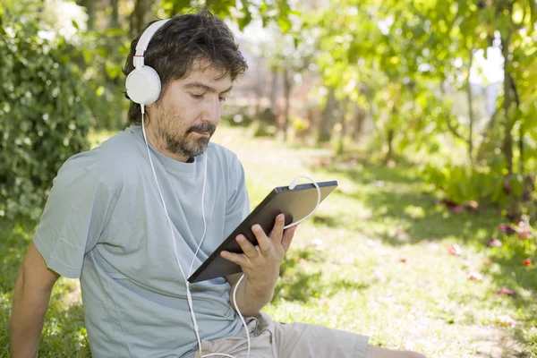 Young man holding a tablet with headphones, outdoor — Stock Photo, Image