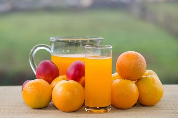 Glazen sinaasappelsap en een heleboel fruit op houten tafel buiten — Stockfoto