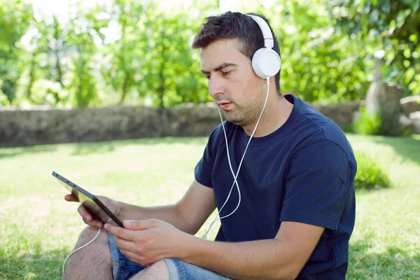 Young man holding a tablet with headphones, outdoor — Stock Photo, Image