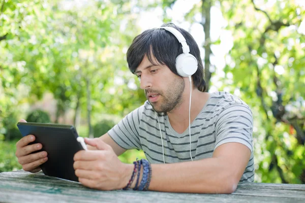 Giovane che lavora con un tablet pc ascoltando musica con le cuffie — Foto Stock
