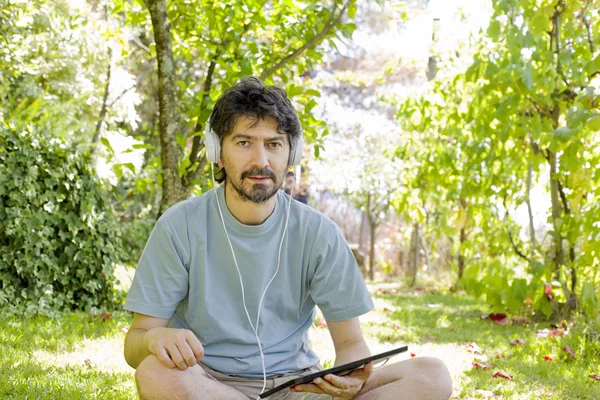 Hombre casual sosteniendo una tableta con auriculares, al aire libre — Foto de Stock