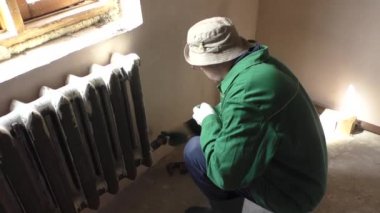 Bir adam bir somun boru demir radyatör üzerinde tutar.