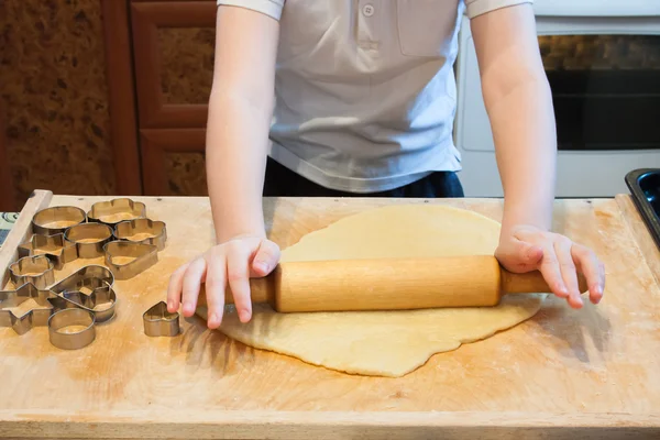 The boy rolls the dough with a rolling pin for  biscuits