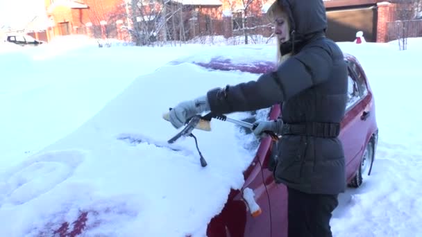 Mujer limpia la nieve de un coche cubierto de nieve — Vídeo de stock