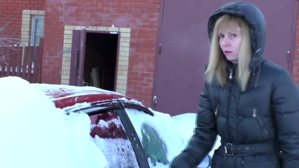 Mulher limpa a neve de um carro coberto de neve — Vídeo de Stock