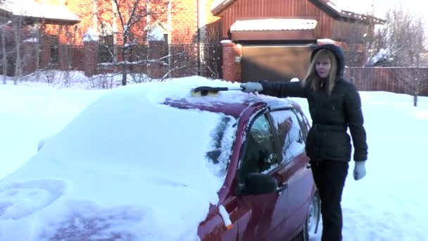 Mulher limpa a neve de um carro coberto de neve — Vídeo de Stock