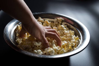 Çocuk el siyah arkaplanda, monitöre karşı kovadan patlamış mısır alıyor.