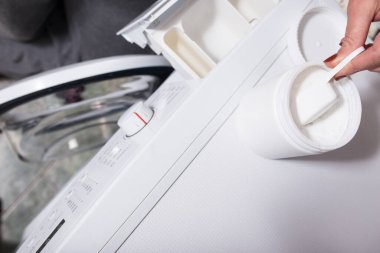 Kadının elleri çamaşır makinesine toz koyuyor..