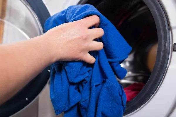 Woman\'s hand load a washing machine with blue colour clothes.