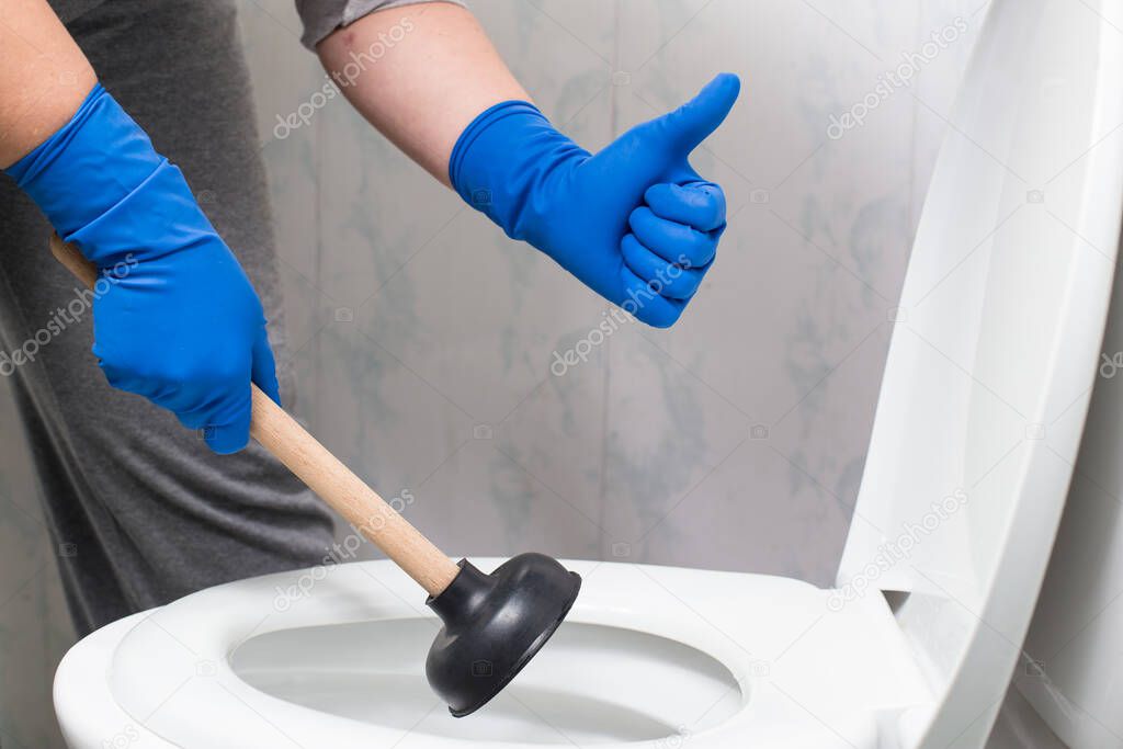 Hands in gloves holding suction cup and showing thumb up near by toilet bowl.