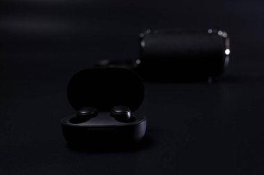 Arka planda kablosuz hoparlör olan siyah kablosuz kulaklıklar şarj ediliyor.