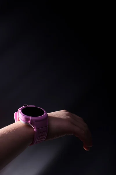Pink children\'s smart watch on hand on black background with copyspace.