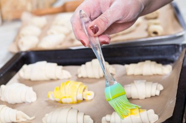 Bir kadının eli ekmek kağıdında çiğ kruvasan fırçalıyor..