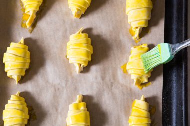 Çiğ Crissantlar, hamur fırçasıyla ışıl ışıl metal tepside pişirmeye hazırlar..