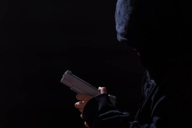 Yüzü kapüşonlu, siyah arka planda fotokopi alanı olan silahlı küçük bir çocuk..