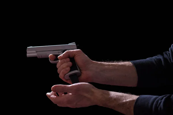 Male hands reloading gun magazine, isolated on blackbackground.