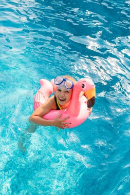 Little girl having fun in a pool with inflatable ring and diving glasses.