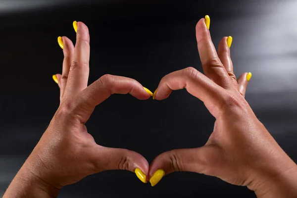 Kobiece Ręce Żółtym Manicure Kształt Serca Czarnym Tle — Zdjęcie stockowe