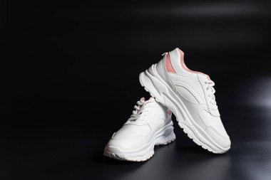 Girl's style white with pink sneakers on black background with copy space.