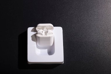 Siyah arkaplanda şarj edilen kablosuz kulaklıklar ve kopyalama alanı.