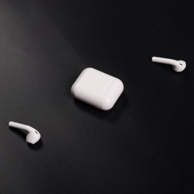 Beyaz kablosuz kulaklıklar siyah arkaplanda şarj davasıyla kapanır..