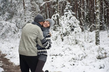 Mutlu çift, karlı ormanda yürürken sarılıyor.