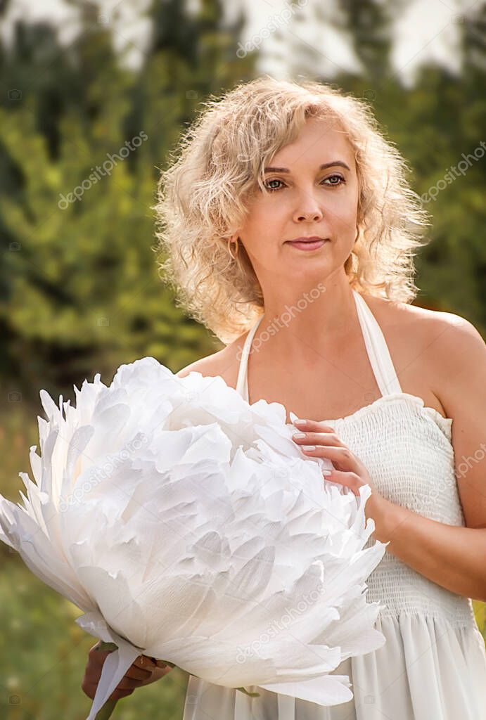curly blonde woman with a large white peony flower in her hands. light, airy image of a woman.