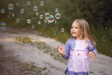 Küçük kız yazın sokakta sabun köpüğüyle oynarken güler..