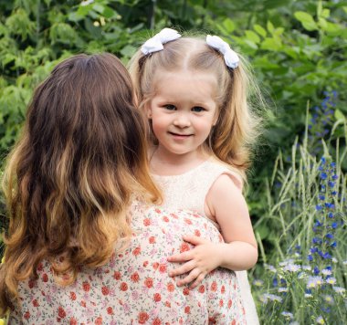 Anne küçük kızını doğada kollarında tutuyor.