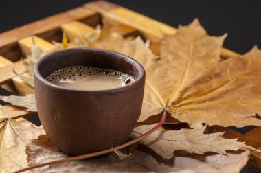 Kahve fincanı ve ahşap bir masa üzerinde sonbahar yaprakları.