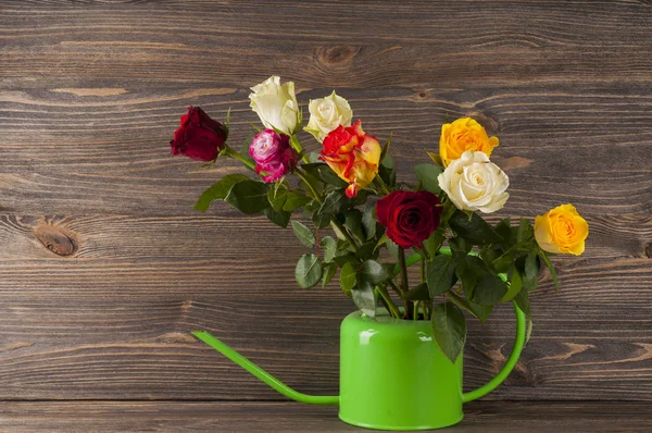 Strauß mehrfarbiger Rosen in der Gießkanne über hölzernem Hintergrund — Stockfoto