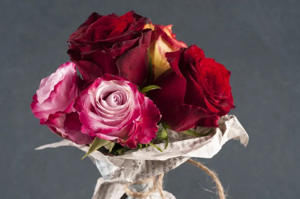 Bando de flores cor de rosa multicoloridas embrulhadas em jornal sobre cinza — Fotografia de Stock