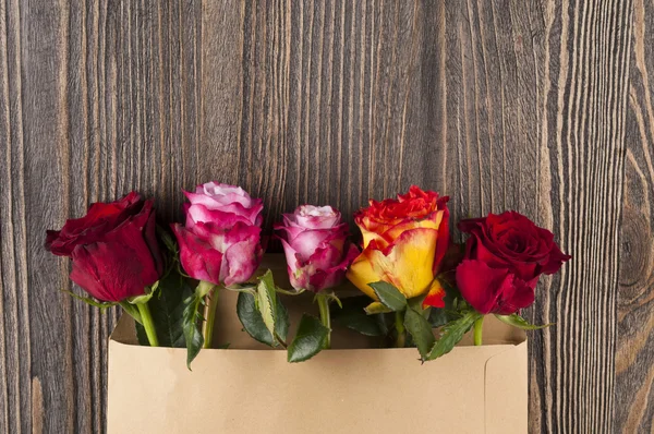 Kilka kwiatów róży multicolor w koperty papierowe na drewniane b — Zdjęcie stockowe