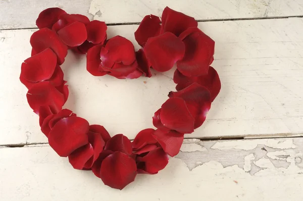 Herz aus roten Rosenblättern auf einem hölzernen Hintergrund. — Stockfoto