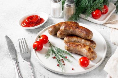 Kızarmış sosis. Baharatlı kızarmış sosis, sos, domates ve maydanoz. Açık gri bir masada beyaz seramik tabakta nefis et sosisleri. Alman yemeği.