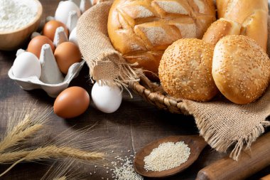 Buğday ekmeği. Buğday ekmeği pişirme malzemeleriyle çevrilidir. Ekmek yakın çekim. Yumurta, tuz, un, mutfak masasındaki tohumlar.