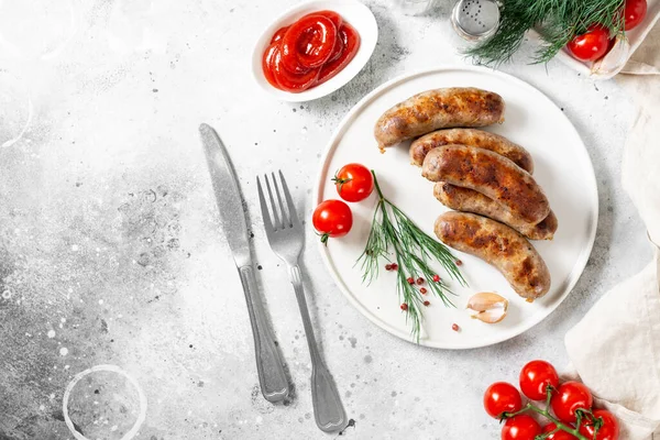 Kızarmış sosis. Baharatlı kızarmış sosis, sos, domates ve maydanoz. Açık gri bir masada beyaz seramik tabakta nefis et sosisleri. Alman yemeği.