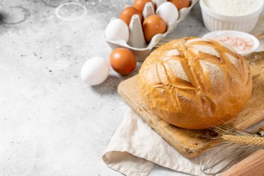 Buğday ekmeği. Buğday ekmeği pişirme malzemeleriyle çevrilidir. Ekmek yakın çekim. Yumurta, tuz, un, mutfak masasındaki tohumlar.